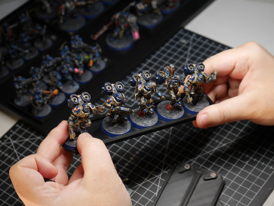 Hands lifting a magnetic tray of blue and gold Space Marine miniatures out of a transport case