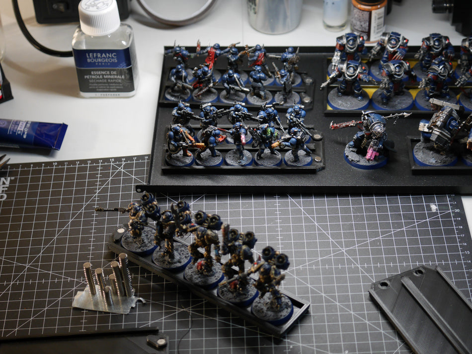 Hobby desk with several magnetic trays of blue Space Marines, magnets and modelling tools